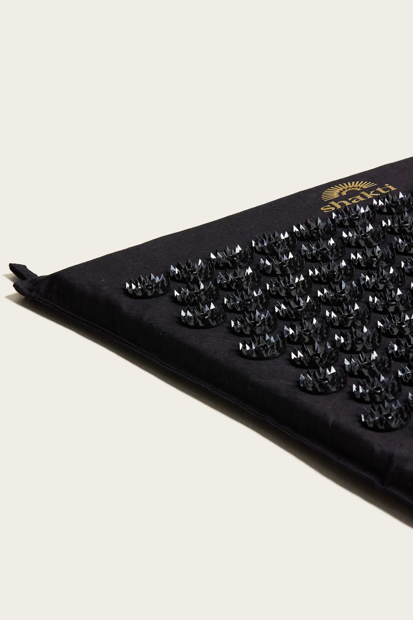 Close up of a Shakti Classic Acupressure Mat showing seams and hanging tabs on a  light background.