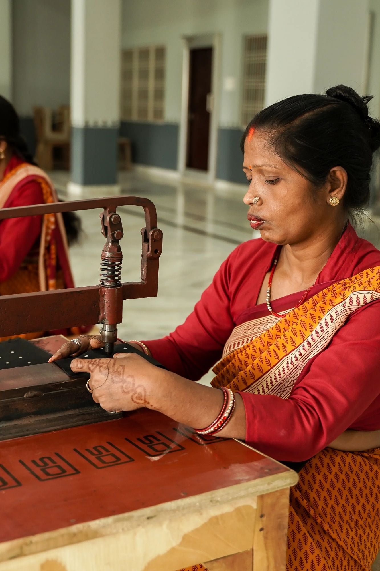 Indian woman using a traditional sewing machine in a workshop setting.